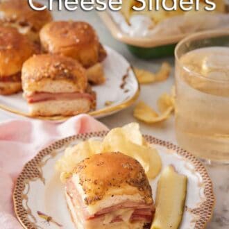 Pinterest graphic of a plate with a ham and cheese slider along with chips and a pickle. More sliders on a platter, chips, and a drink in the background.