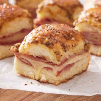 Multiple ham and cheese sliders on a parchment lined serving board.