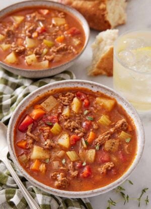 Two bowls of hamburger soup, one in front, with a drink in the background.