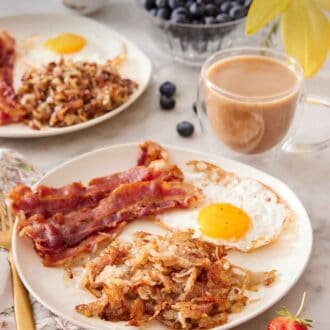 Pinterest graphic of hash browns, bacon strips, and a fried egg on a plate with a cup of coffee, bowl of blueberries, and additional plate in the background.