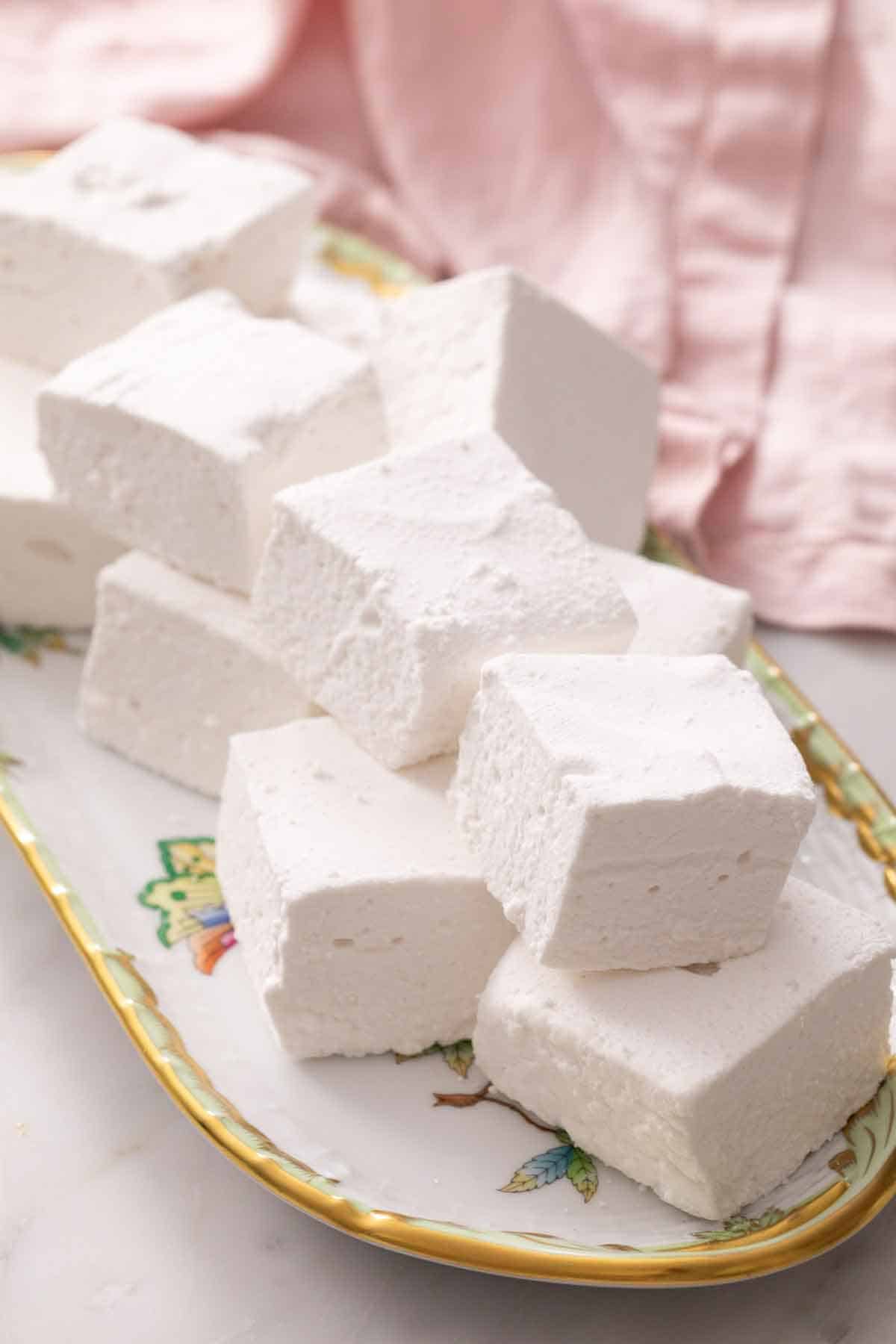 A platter of multiple homemade marshmallows. A pink napkin in the back.