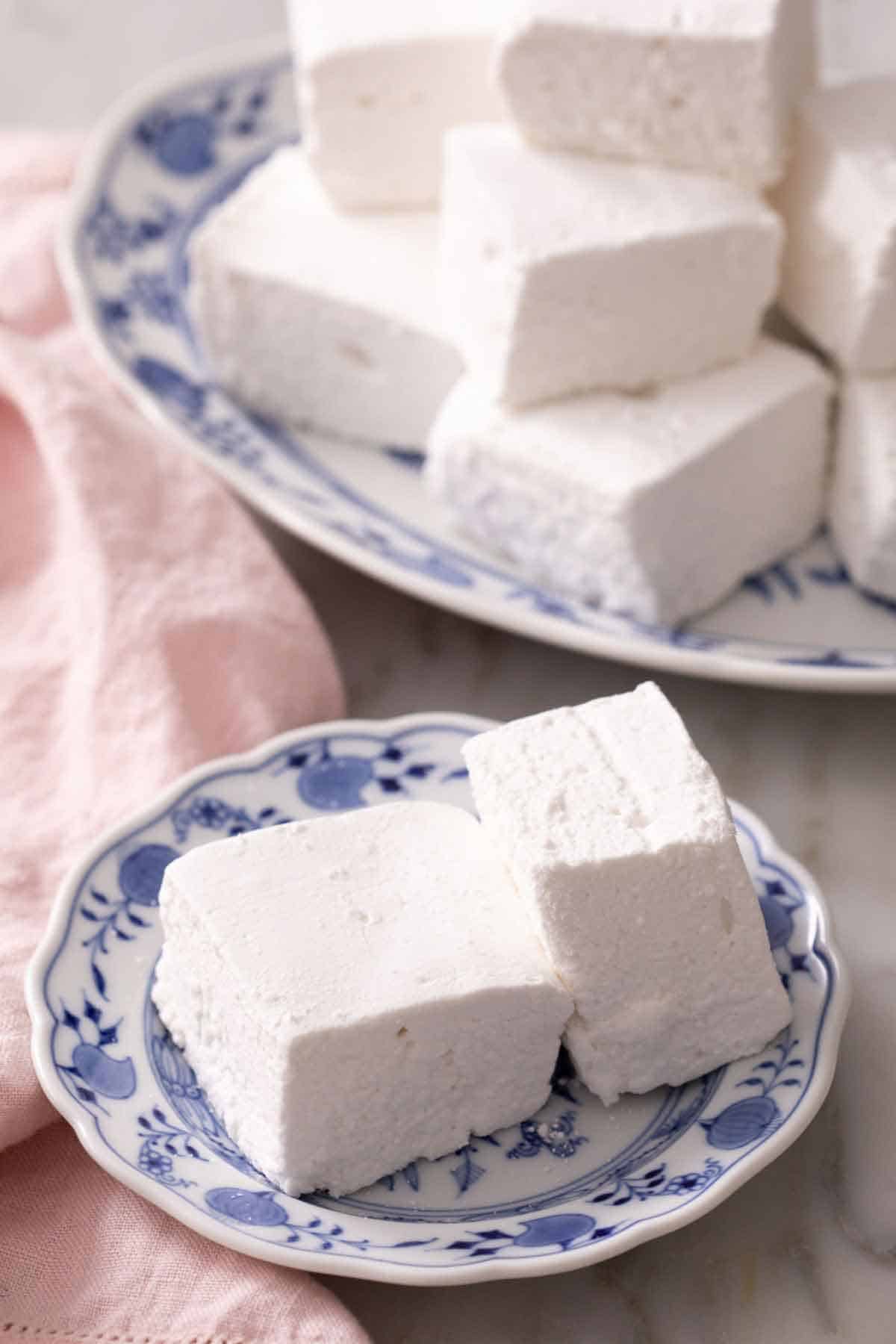A plate with two homemade marshmallows with a platter in the background.