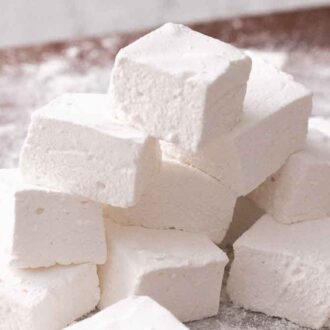 A pile of homemade marshmallows with powdered sugar dusted around it.