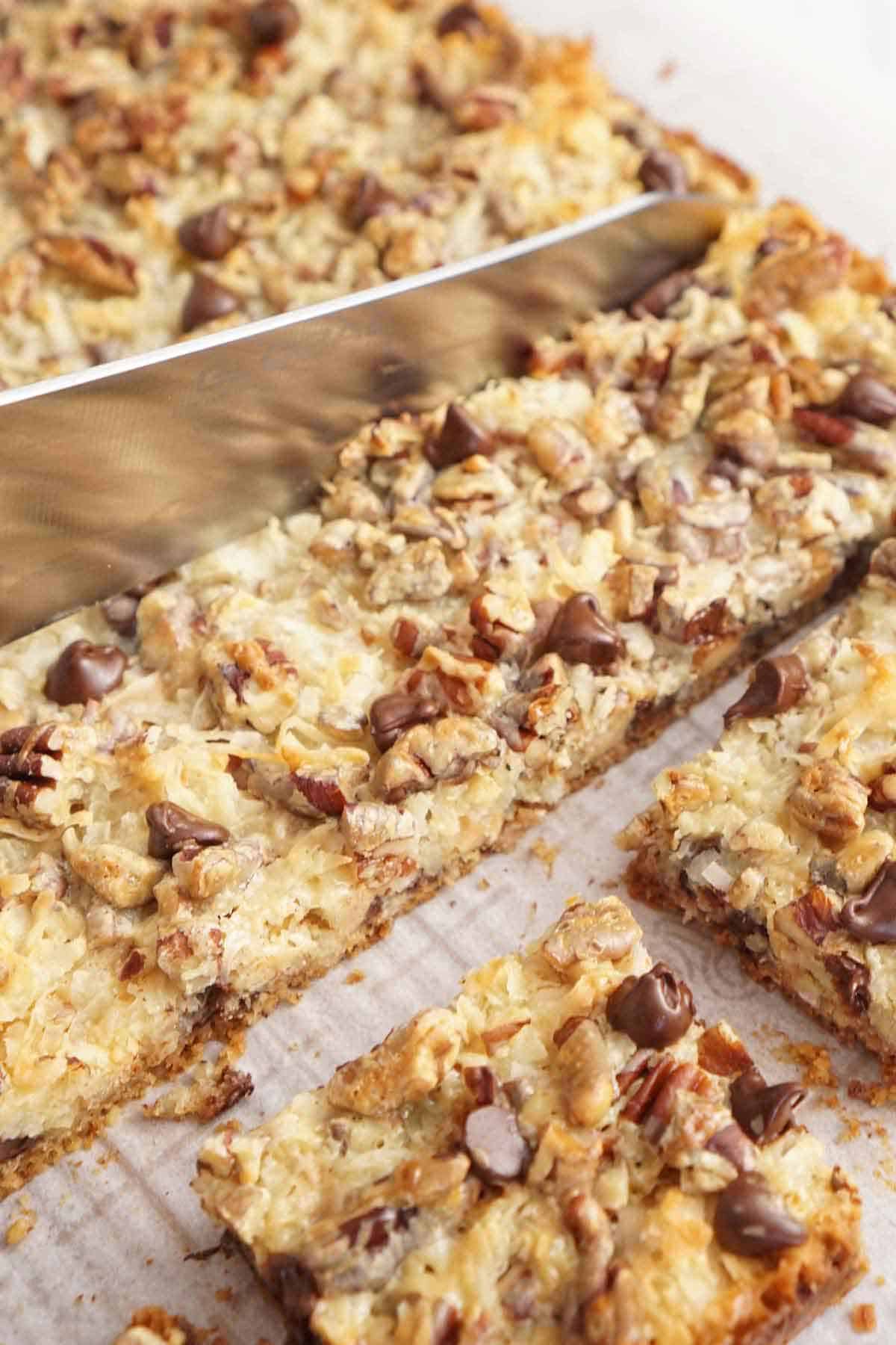 Magic cookie bars being cut with a knife into squares.