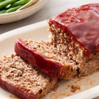 A platter with a loaf of meatloaf with two slices cut.