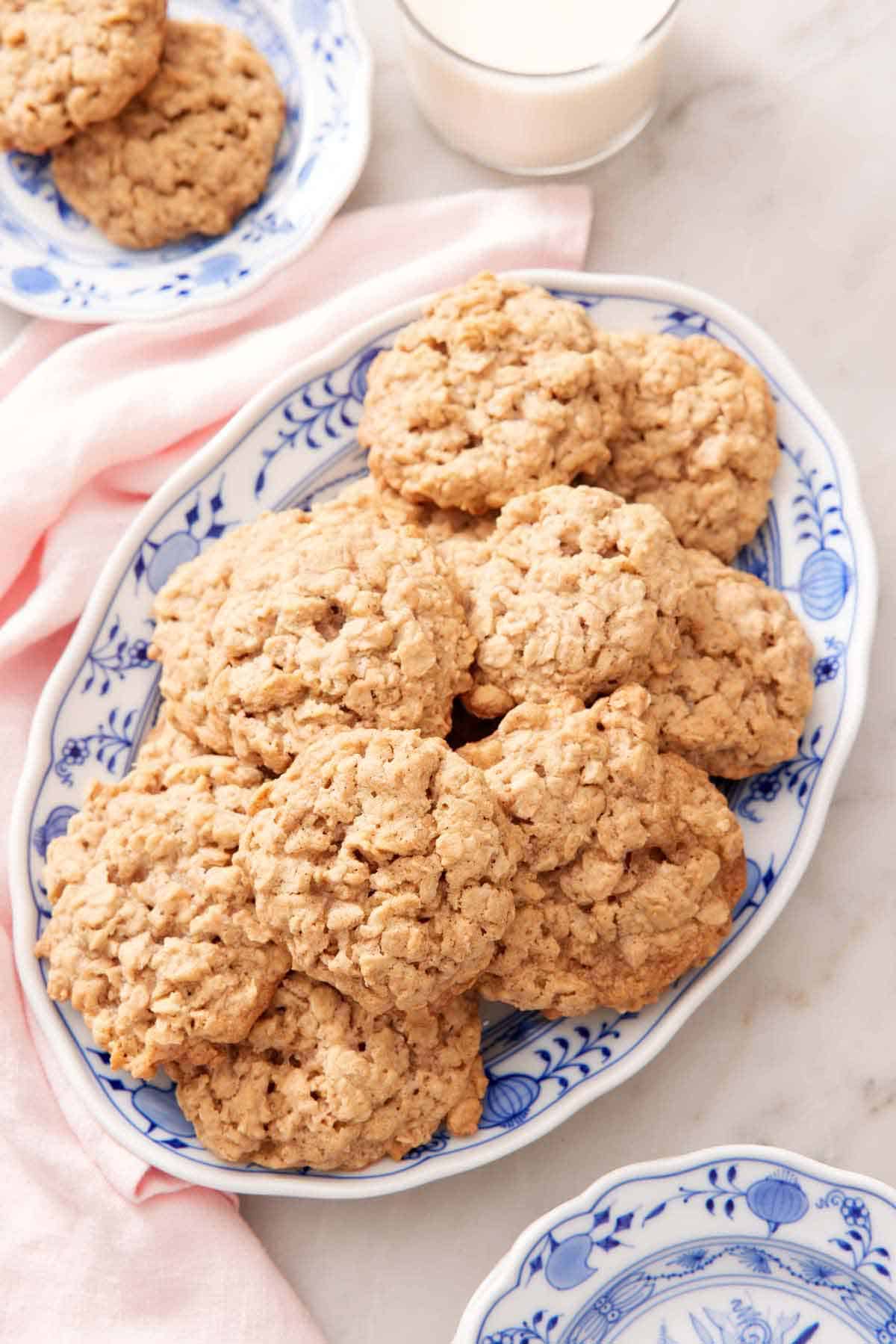 A platter of oatmeal cookies with more on a plate on the side with a glass of milk.