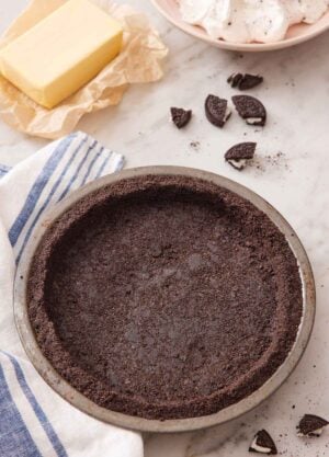 Overhead view of an Oreo pie crust in a pie pan and some Oreos, butter, and whipped topping in the background.