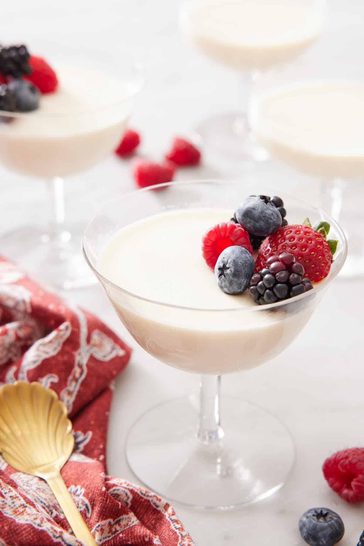 A glass of panna cotta topped with berries with more glasses in the background.
