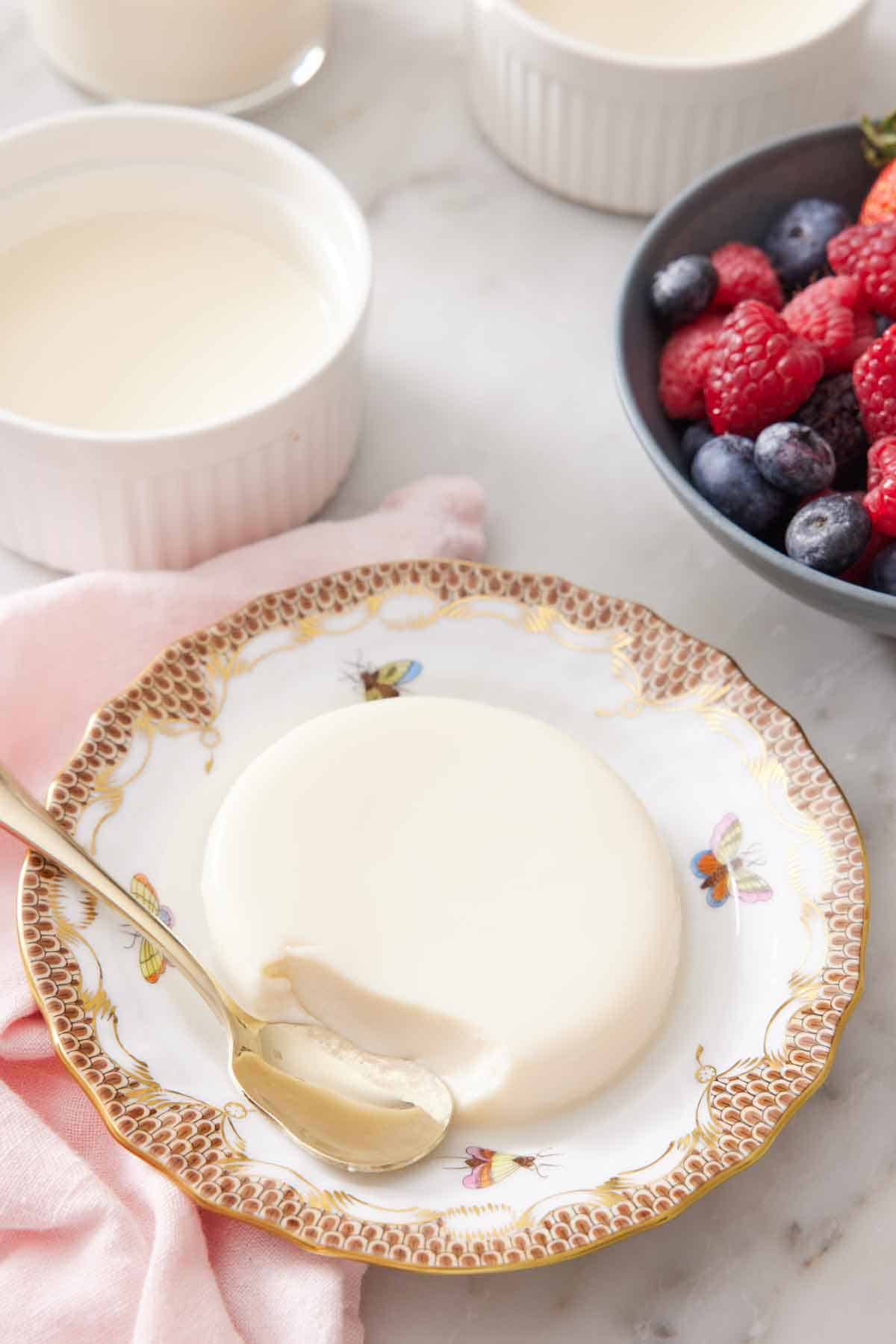 A plate with a serving of panna cotta with a spoon in front of a bite taken.