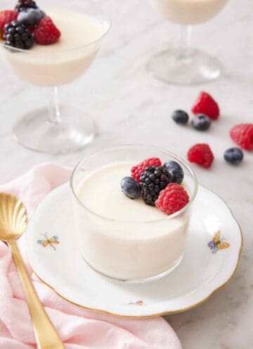 A plate with a glass of panna cotta topped with berries. More cups of panna cotta in the background.