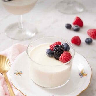Pinterest graphic of a plate with a glass of panna cotta topped with berries.