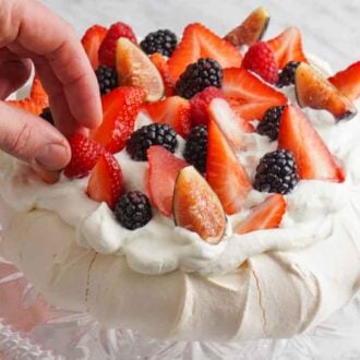 A pavlova on a cake stand with berries being placed on top.