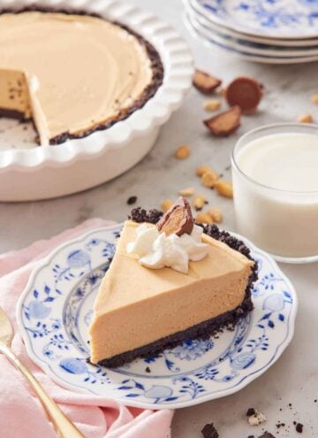 A slice of peanut butter pie with a glass of milk and the rest of the pie in the background.
