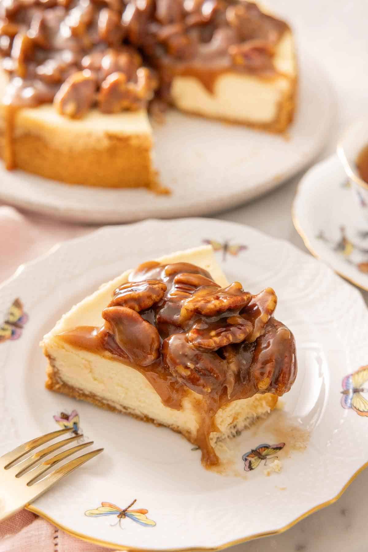 A slice of pecan pie cheesecake on a plate with a bite taken out. Rest of the cheesecake in the background.