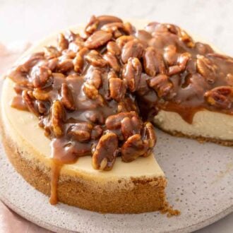 A pecan pie cheesecake on a serving platter with a slice cut out.