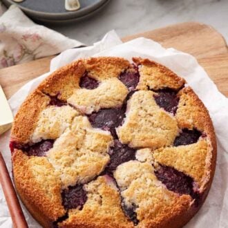 Pinterest graphic of a plum cake on a parchment lined serving board with two plums and plates in the background.