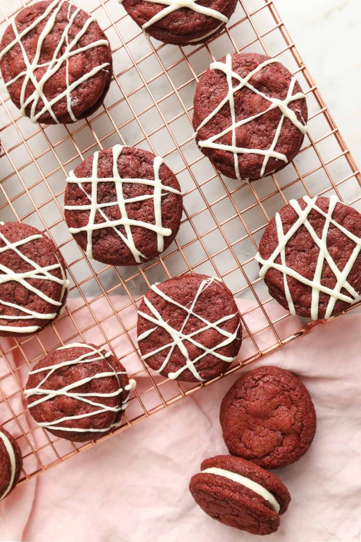 Overhead view of red velvet cookies on a cooling rack topped with drizzles of melted white chocolate.