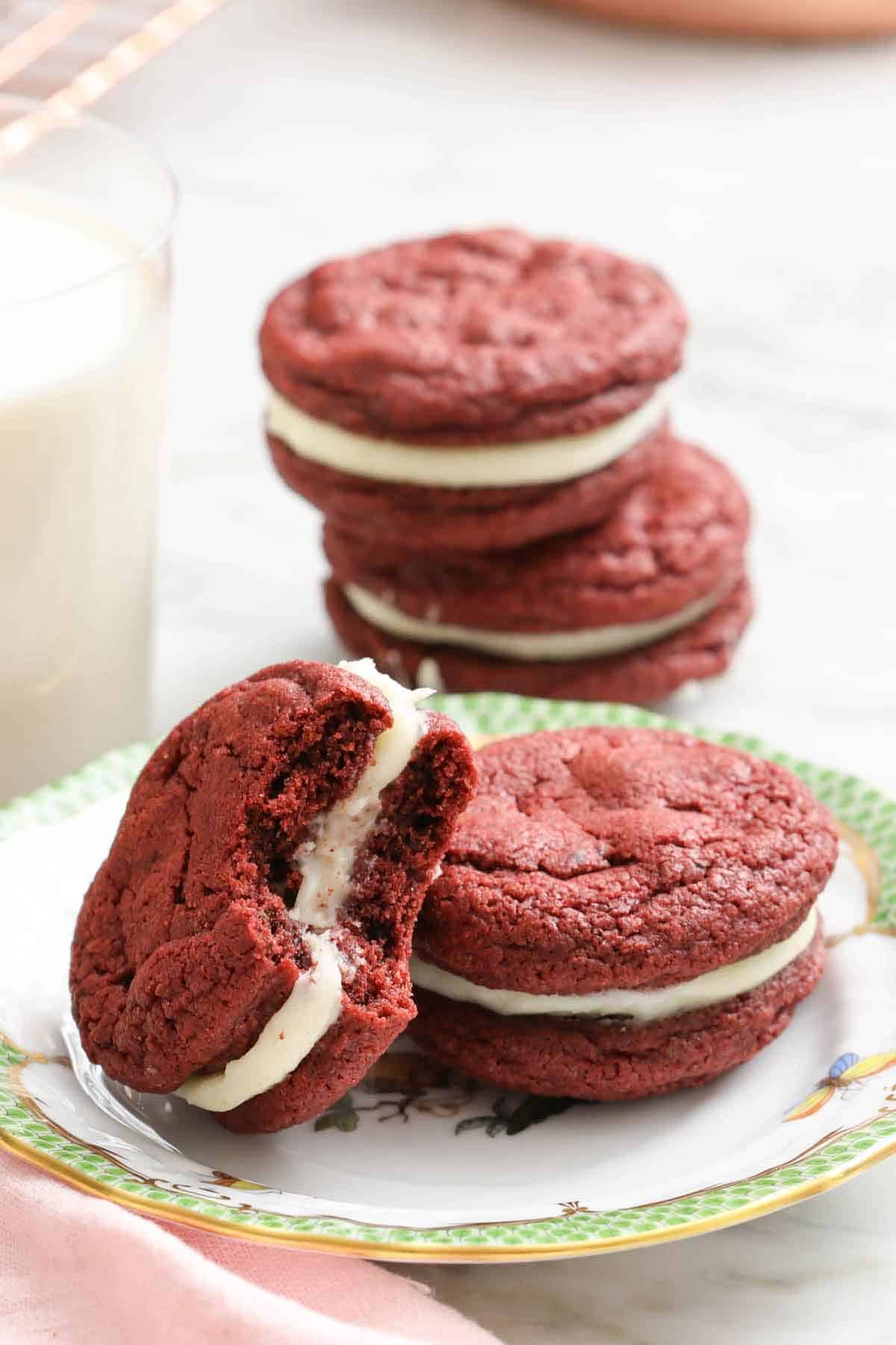A plate with red velvet cookies with one stacked on top of another with a bite taken out of it.