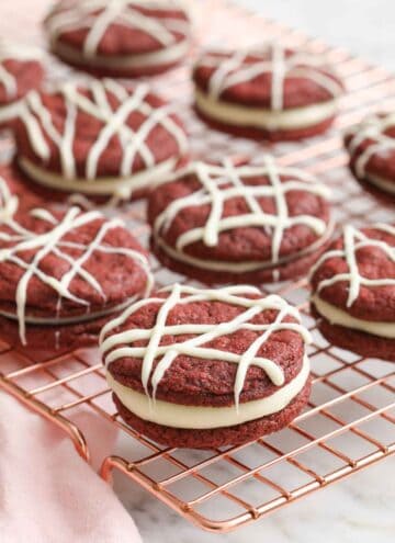 A cooling rack with red velvet cookies topped with drizzles of melted white chocolate.