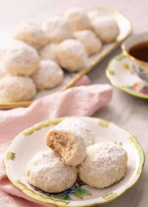 A plate with multiple Russian tea cakes with the one on top with a bite taken out of it. A platter more in the background.
