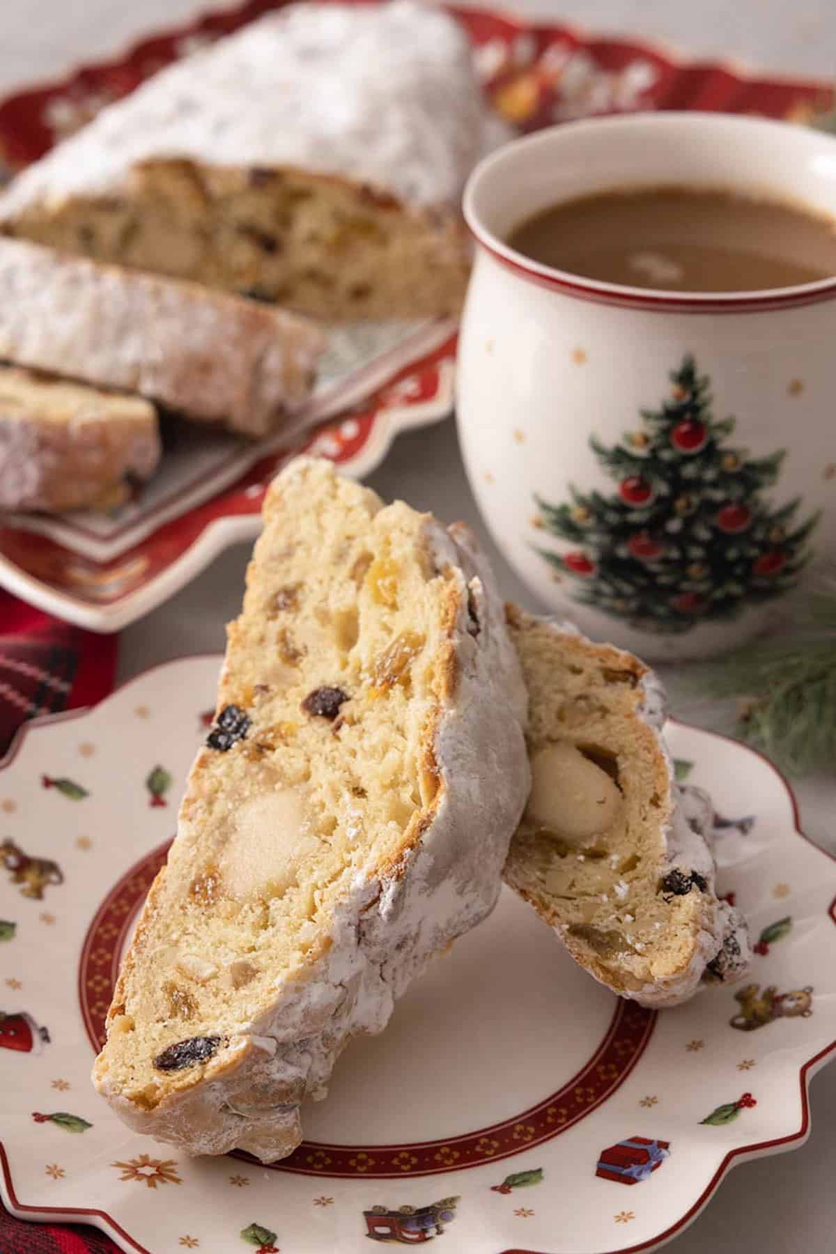 A festive plate with two slices of stollen by a mug of hot chocolate.