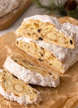 A loaf of stollen, sliced on parchment paper with one slice placed on top of the uncut part of the loaf.