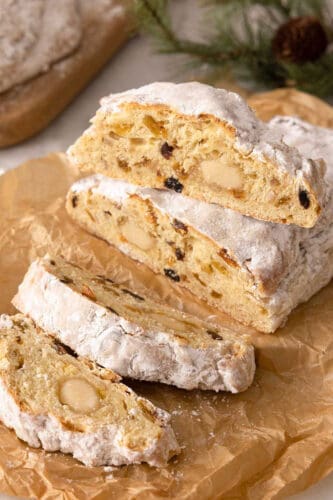 A loaf of stollen, sliced on parchment paper with one slice placed on top of the uncut part of the loaf.