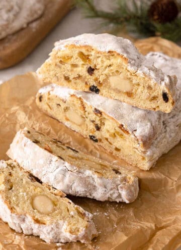 A loaf of stollen, sliced on parchment paper with one slice placed on top of the uncut part of the loaf.