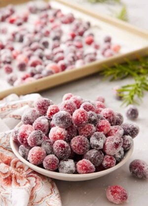 A bowl of sugared cranberries with a sheet pan with more in the background.