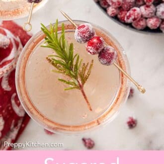 Pinterest graphic of an overhead view of a drink with a rosemary and sugared cranberries garnish. A bowl of more sugared cranberries on the side.