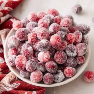 A slightly overhead view of a bowl of sugared cranberries with more scattered around and a linen napkin on the side.