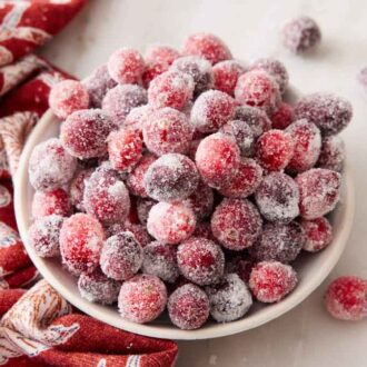 A slightly overhead view of a bowl of sugared cranberries with more scattered around and a linen napkin on the side.