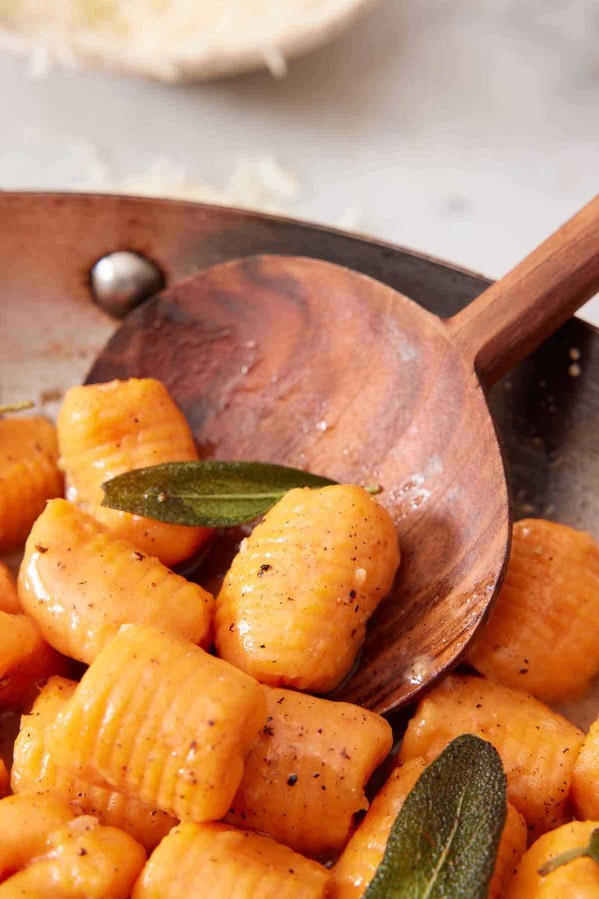 A skillet with sweet potato gnocchi with a serving spoon tucked behind some gnocchi.