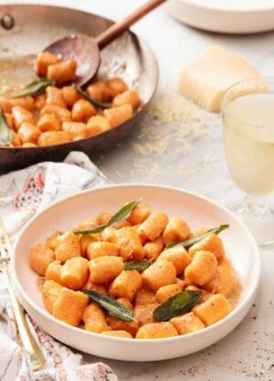 A plate of sweet potato gnocchi with sage leaves. A skillet of sweet potato gnocchi in the background.
