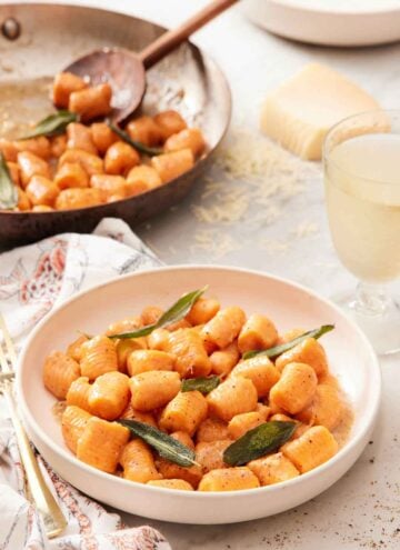 A plate of sweet potato gnocchi with sage leaves. A skillet of sweet potato gnocchi in the background.