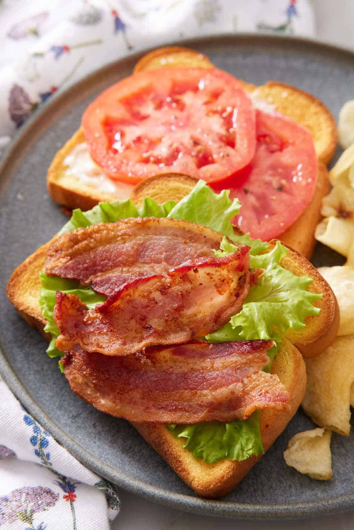 A plate with air fryer bacon on a piece of toast with lettuce and tomatoes on a second toast.