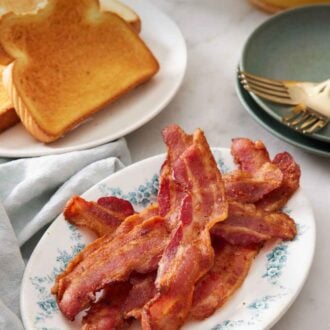 Pinterest graphic of a platter of air fryer bacon with a plate of toast in the background along with a stack of plates and forks.