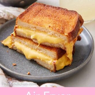 Pinterest graphic of an air fryer grilled cheese cut in half, stacked on top of each other on a plate. A drink and bowl of tomato soup in the back.