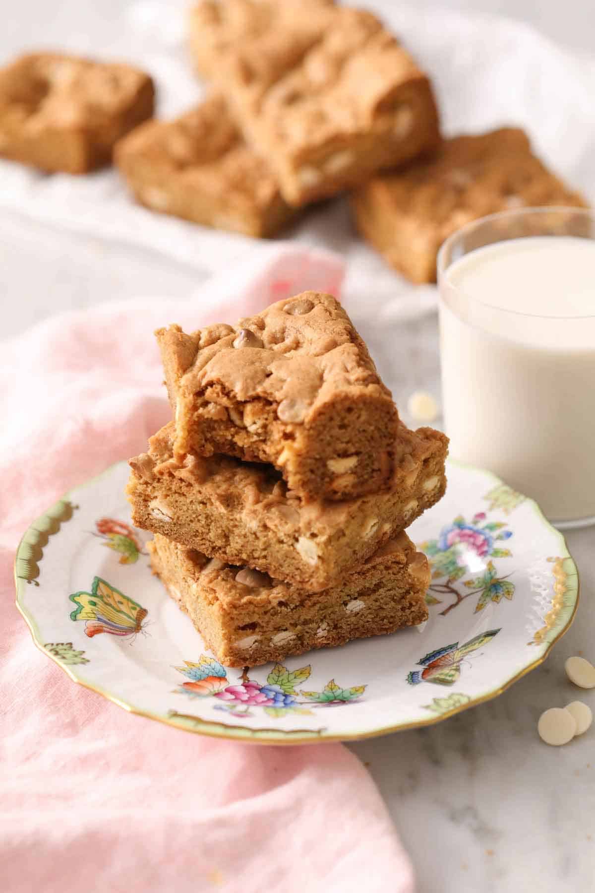 A stack of three blondies on a plate with a glass of milk in the back.