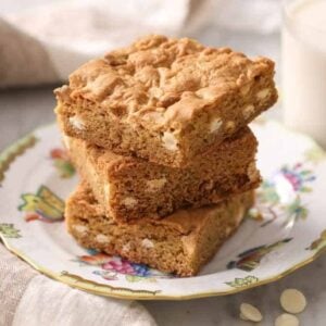 A plate with three blondies with a glass of milk behind it.