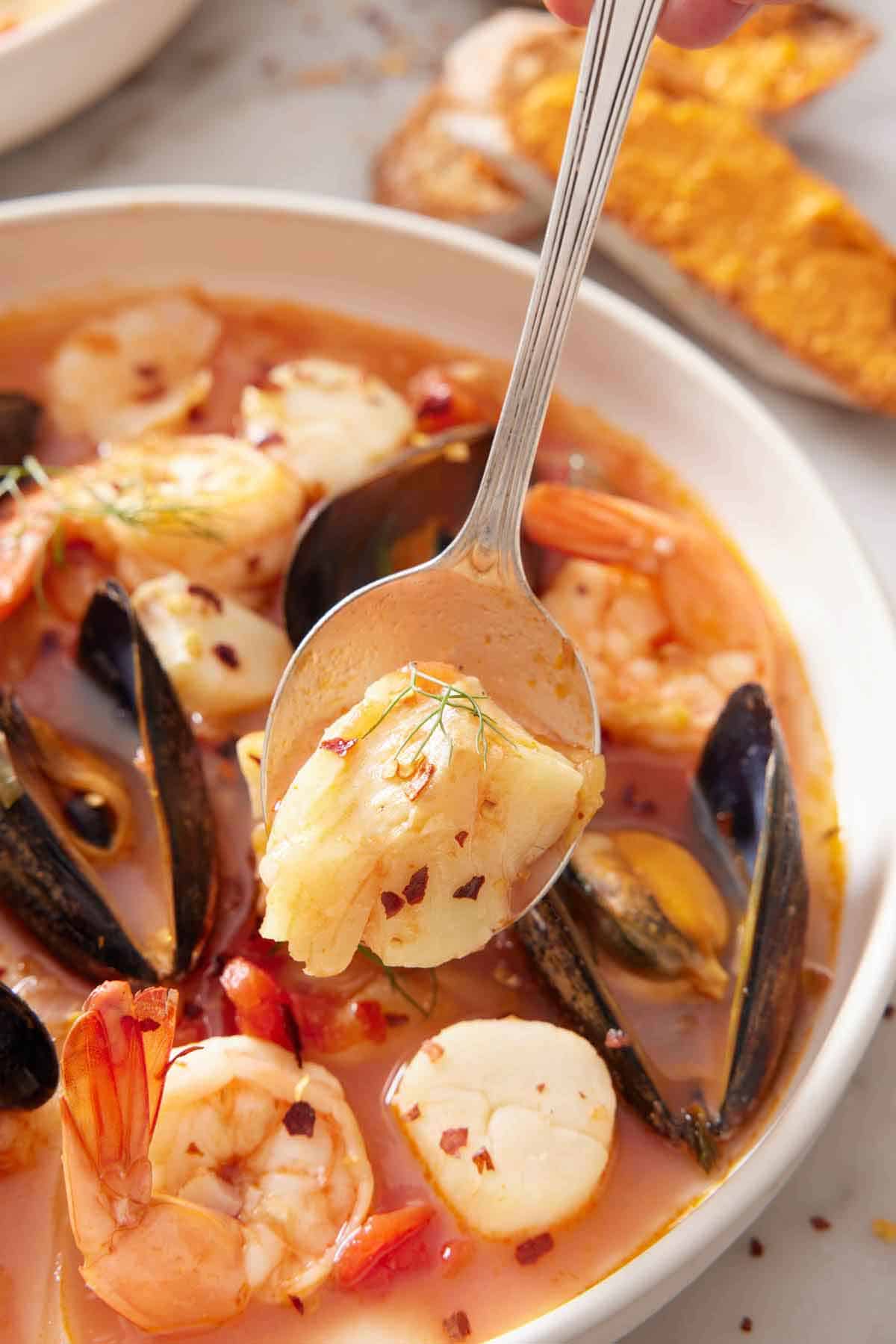 A spoonful lifting up shrimp from a bowl of bouillabaisse.
