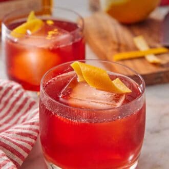 Pinterest graphic of a boulevardier with an orange twist on top. A second glass in the background along with an orange.