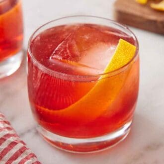 A glass with boulevardier with a large ice cube and orange twist.