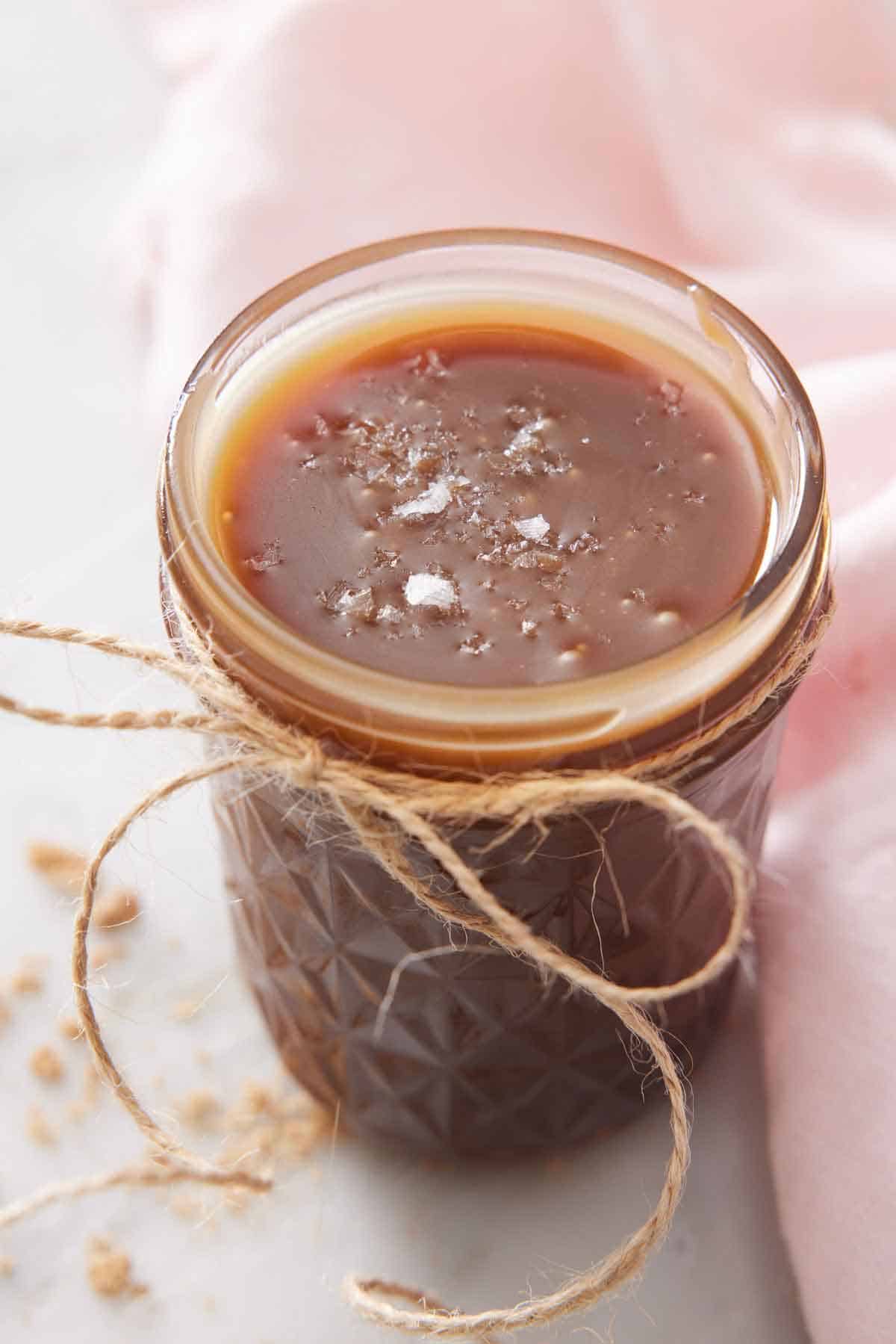 A jar of butterscotch with a twine bow tied on and flaky sea salt on top.