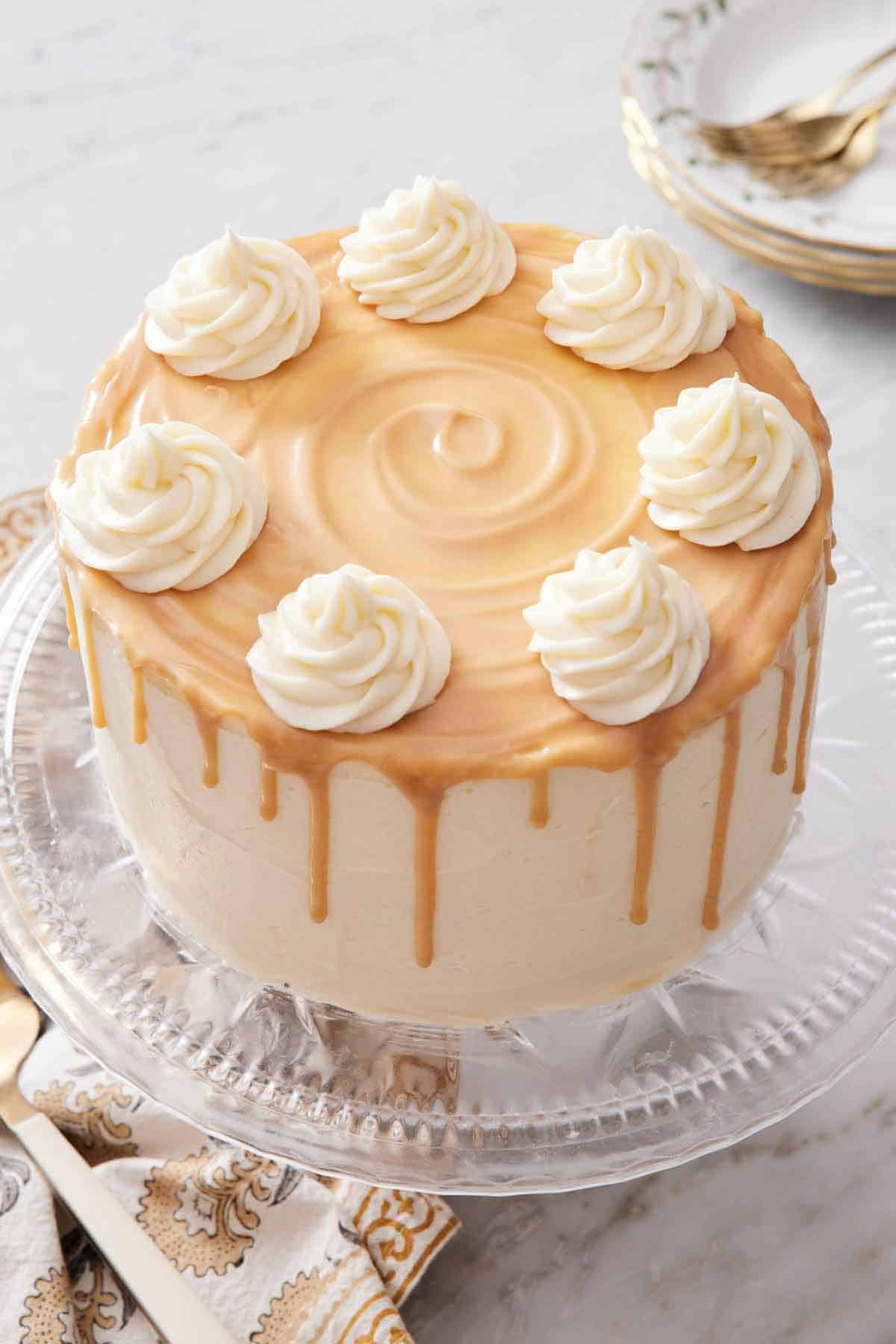 A butterscotch cake on a cake stand, topped with dollops of frosting over a layer of butterscotch.