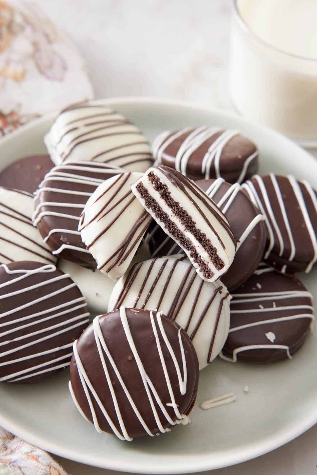 A platter of chocolate covered oreos with one cut in half showing the interior.