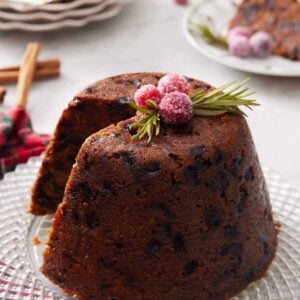 A platter with a Christmas pudding with a slice cut out with sugared cranberries and rosemary on top.