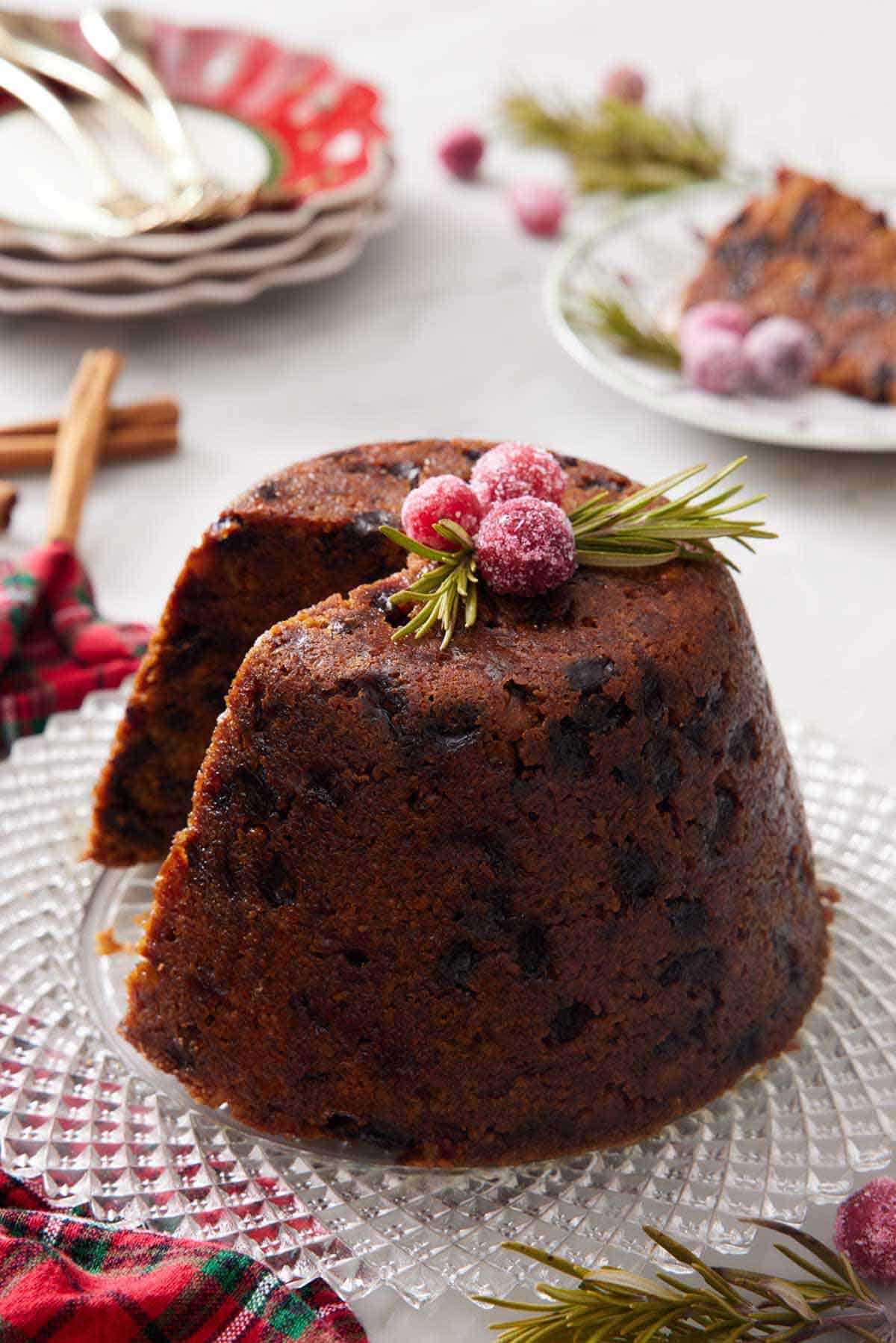 A platter with a Christmas pudding with a slice cut out with sugared cranberries and rosemary on top.