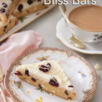 Pinterest graphic of a plate with a slice of cranberry bliss bar with a coffee and platter with more bars in the background.