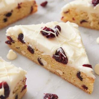Cranberry bliss bars on a counter with white chocolate chips and dried cranberries scattered around.